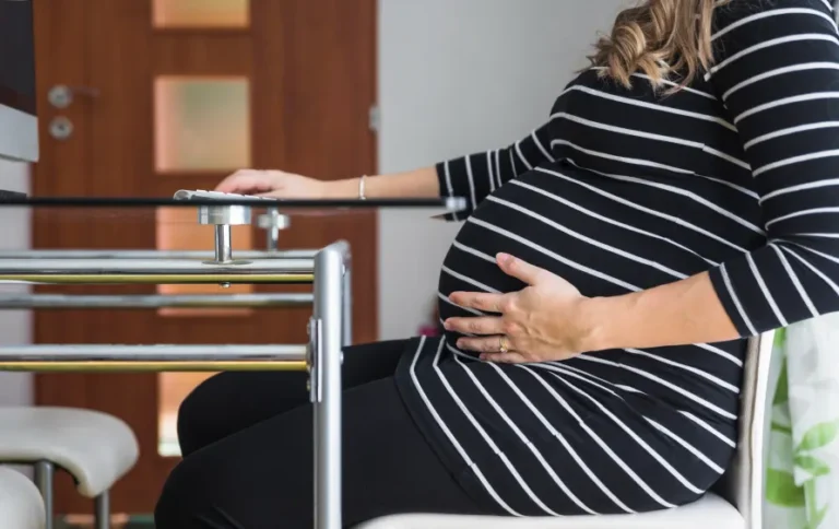 Pregnant woman sitting on a chair experiencing tailbone pain during pregnancy