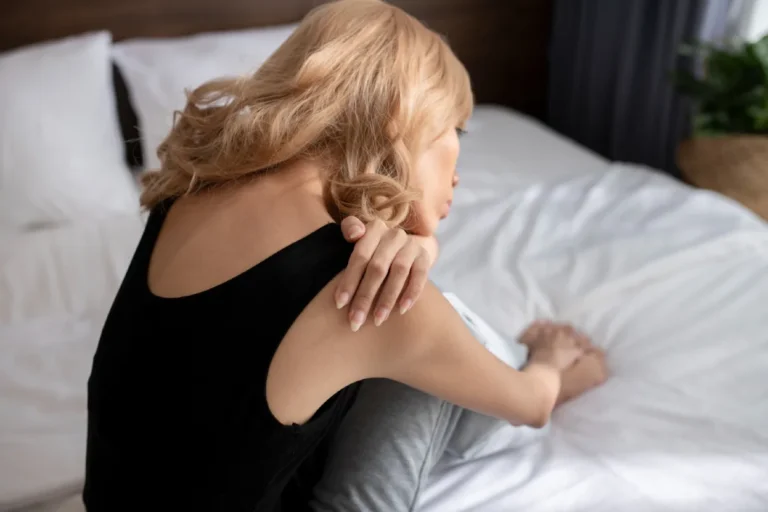 Woman in bed holding her shoulder due to shoulder pain at night.