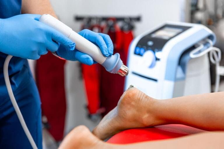 Patient receiving extracorporeal shockwave therapy (ESWT) applied to the heel for treatment of plantar fasciitis using a handheld device on the plantar fascia.